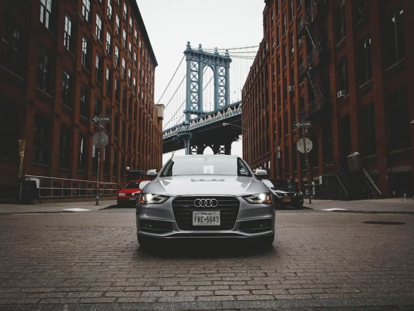 Silver Audi A4 parked on cobblestones in DUMBO, Brooklyn with the Manhattan Bridge towering behind it